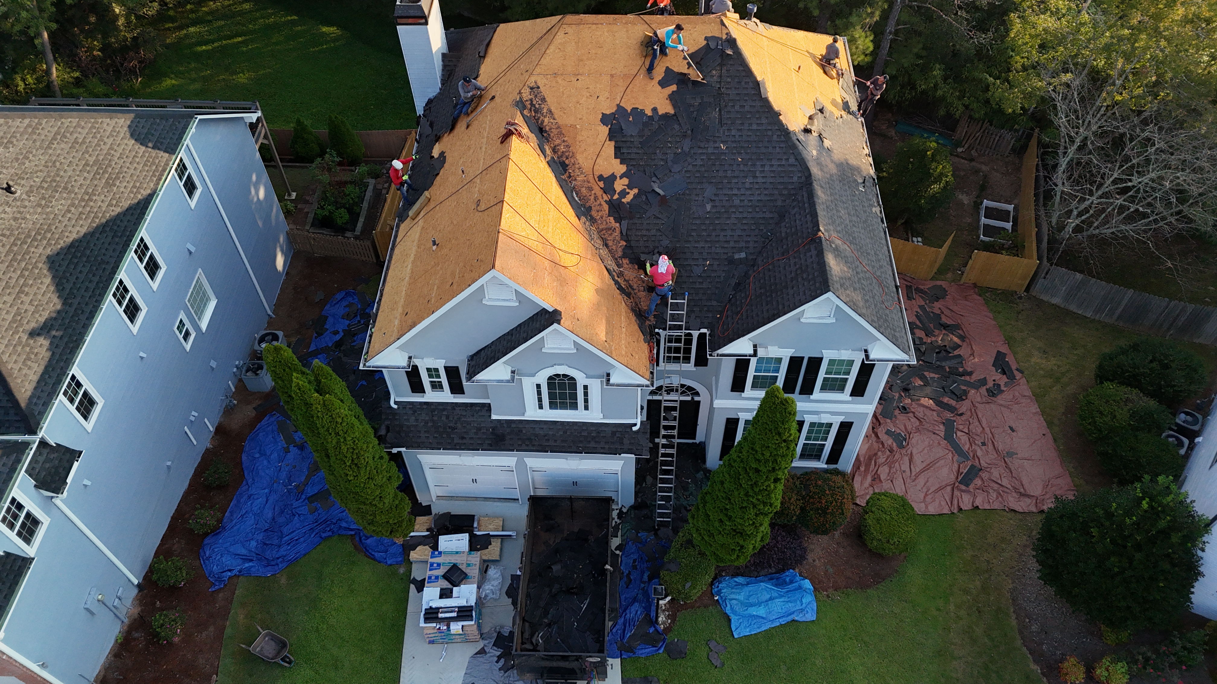 Aerial view of roofing crew replacing shingles on large white home